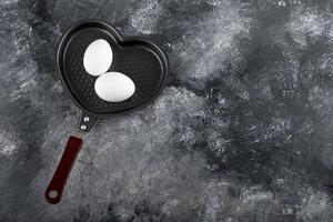 dos huevos blancos en una sartén en forma de corazón foto