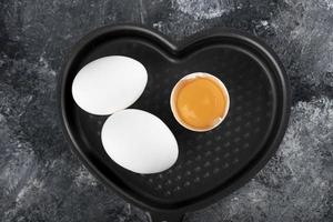 Two white eggs and yolk on a heart-shaped pan photo