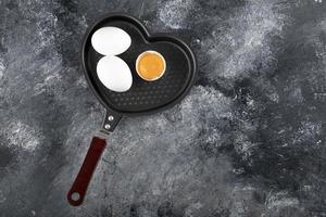 Two white eggs and yolk on a heart-shaped pan photo