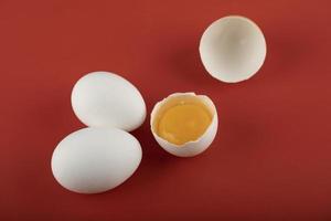 Broken and whole raw eggs on a red background photo