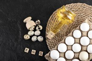 Fresh farm quail eggs, chicken eggs, and olive oil with wooden blocks with the word Egg on a black background photo