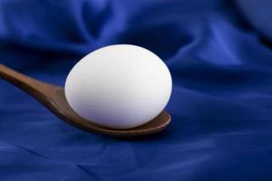 Single raw egg with a wooden spoon on a blue satin cloth photo