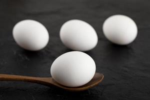 Huevos blancos crudos y una cuchara de madera sobre un fondo negro foto