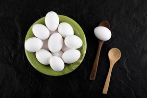 Bunch of raw eggs on a green plate with wooden spoons photo