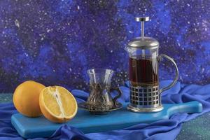 Glass of tea, orange, and tea pot on a blue board photo