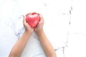 Child's hand holding red heart on white marble background photo