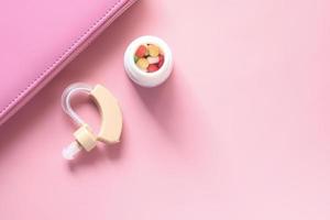 Hearing aid and pills on pink background photo