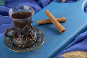 un té de vidrio con ramas de canela en una tabla de cortar de madera foto