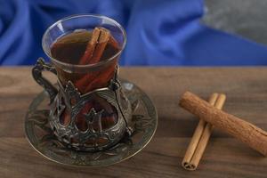 un té de vidrio con ramas de canela en una tabla de cortar de madera foto