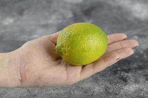 mano de mujer sosteniendo un limón verde fresco
