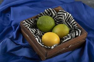 A wooden basket with three lemons on a blue cloth photo