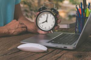 A person's hand holding a clock at a work desk photo