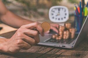 A person using a computer with a stack of coins, make money online concept photo