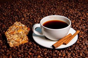 White coffee mug, cinnamon sticks and cookies on the coffee beans background photo