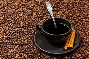 Taza de café negro y palitos de canela en el fondo de los granos de café foto
