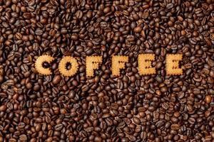 La palabra café hecha de letras de galletas sobre un fondo de grano de café oscuro foto