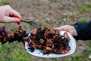 la mano humana sostiene un plato blanco de kebab recién horneado foto