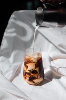 barista vertiendo leche en un vaso de café helado foto