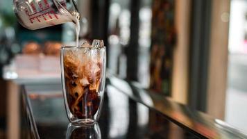 barista vertiendo leche en un vaso de café helado foto