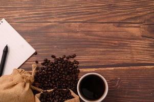 café, granos de café y un cuaderno con un bolígrafo en un escritorio de madera foto