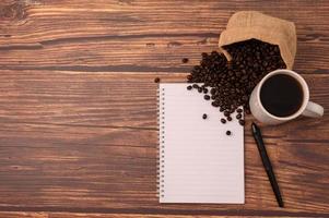 Coffee, coffee beans, and a notebook with a pen on a wooden desk photo