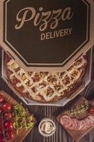 Pizza with mozzarella, calabrese sausage, eggs, catupiry, olive and oregano in a delivery box photo