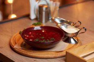 A Ukrainian borsch with a pampushka, onion, and sour cream on a wooden tray photo