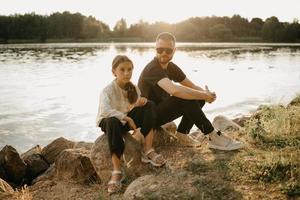 A young father with a beard and sunglasses is posing with his pretty daughter on the coast photo