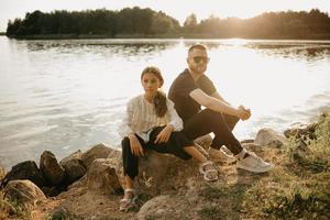 A young father with a beard and sunglasses is posing on stones with his daughter on the coast photo