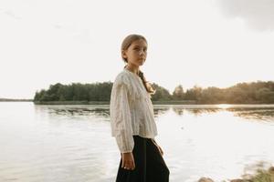 A blurred portrait of a young girl who is walking on the coast of the lake on the sunset photo