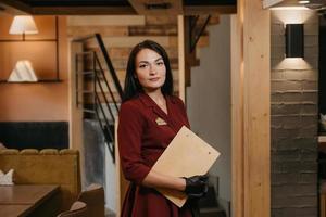 A female restaurant manager in black disposable medical gloves holding a wooden menu in a restaurant photo