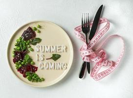 A plate with a salad with the word Summer is Coming on a white textured background photo