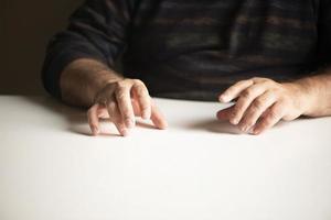 Hombre irreconocible en una posición familiar sentado en una mesa blanca vacía foto