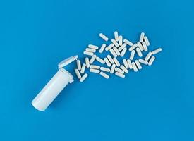 White plastic medical bottle and scattered pill capsules on a blue backdrop photo