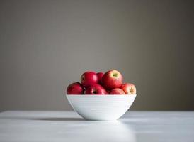 Red apples fruits on white table bowl gray background