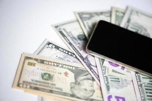 Dollar banknotes and black smartphone on white background, top view photo