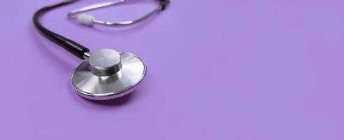 Black stethoscope on a purple background with copy space