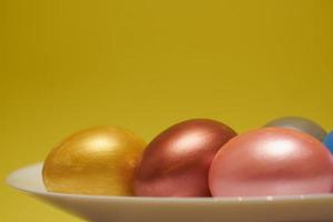 Painted eggs on a white plate with a yellow background for Easter photo