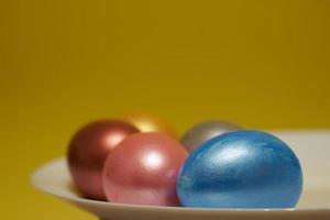 Painted eggs on a white plate with a yellow background for Easter photo