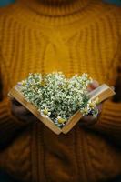 Woman's holding a book with daisies inside photo