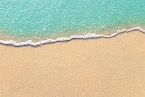 Soft waves with foam of blue ocean on the sandy beach photo