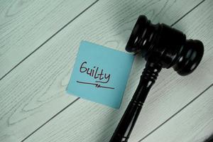 Guilty written on notepad with gavel isolated on wooden table photo