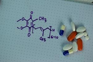 Vitamin coenzyme Q10 with chemical formula written on a book isolated on wooden table photo