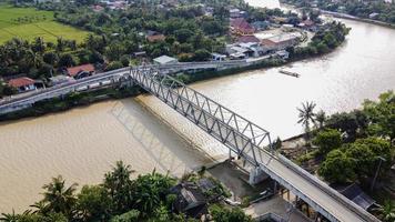 Bekasi, Indonesia 2021- Aerial drone view of a long bridge to the end of the river connecting  two villages photo