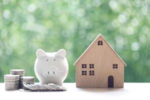 Model house with piggy bank and stack of coins on natural green background photo