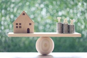 Model house with stack of coins and tax word on seesaw green background photo