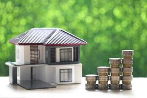 Model house and stack of coins money on natural green background photo