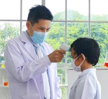 Teachers using an infrared forehead thermometer to check the temperature of a male student before going to class photo