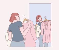 una mujer sostiene un vestido y se mira en el espejo. vector