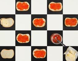 Salmon caviar canapes, butter, red caviar in a jar forming a pattern on chess board, top view photo